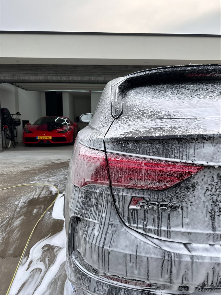 Rear view of a wet silver SUV with red taillights in a garage, with a red sports car visible in the background