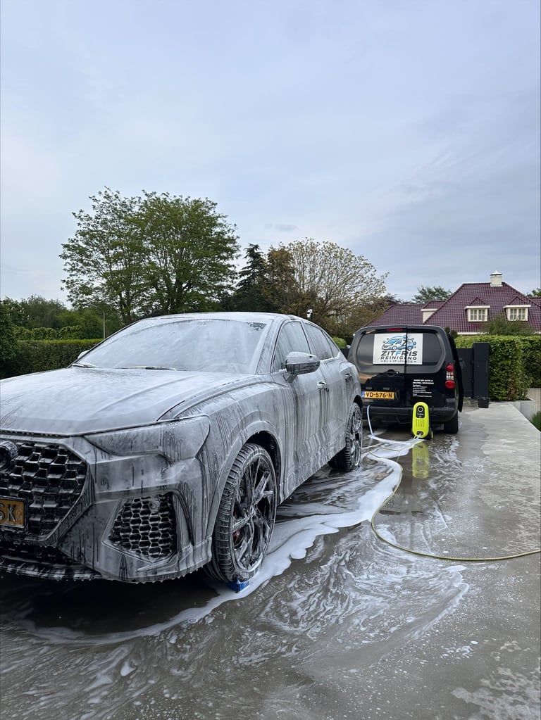 Luxury car being professionally washed with high-pressure water spray in a residential driveway