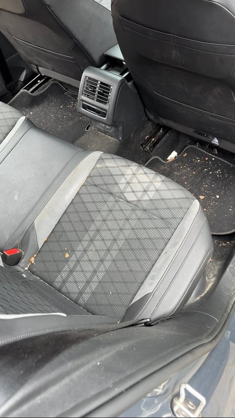 Interior view of car back seat with gray upholstered cushion, air vent, and black leather seats